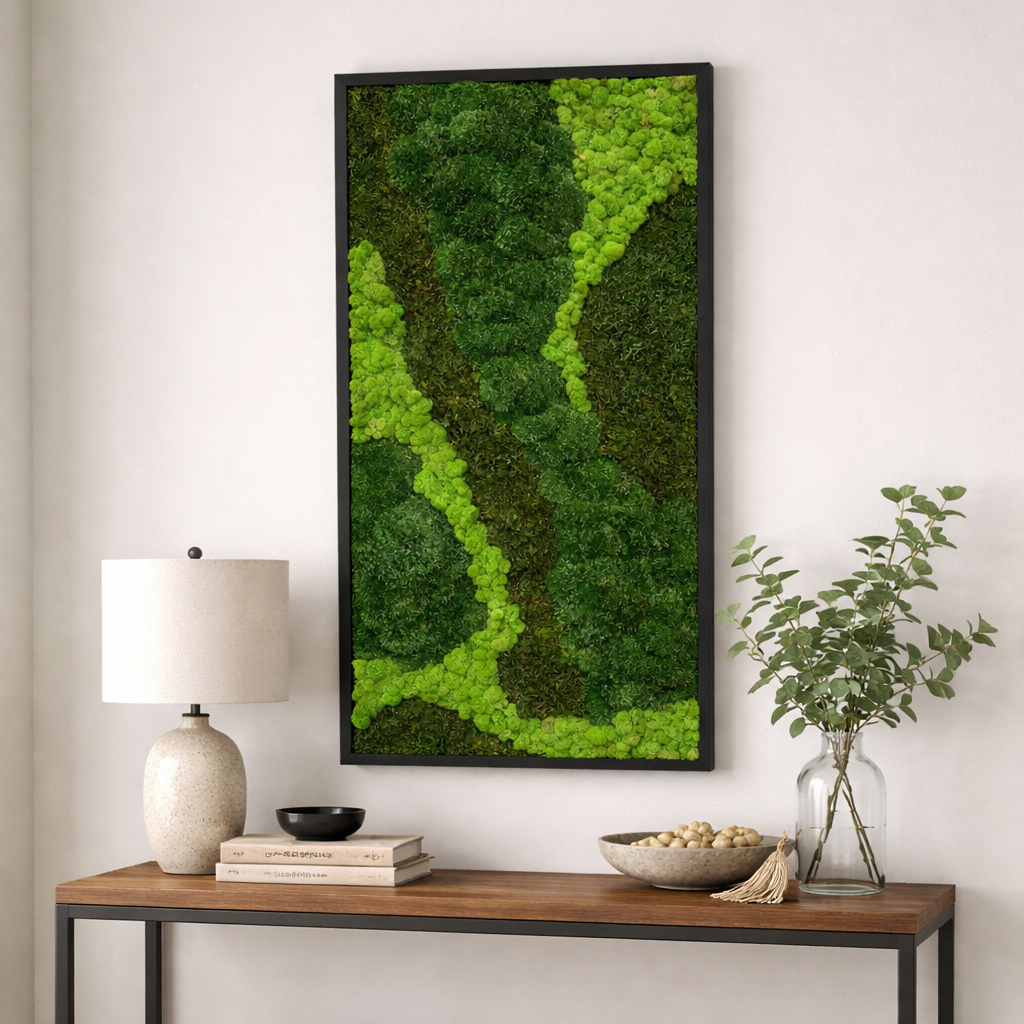 Vertical green moss artwork in a black frame above a wood console, styled with a lamp and vase.