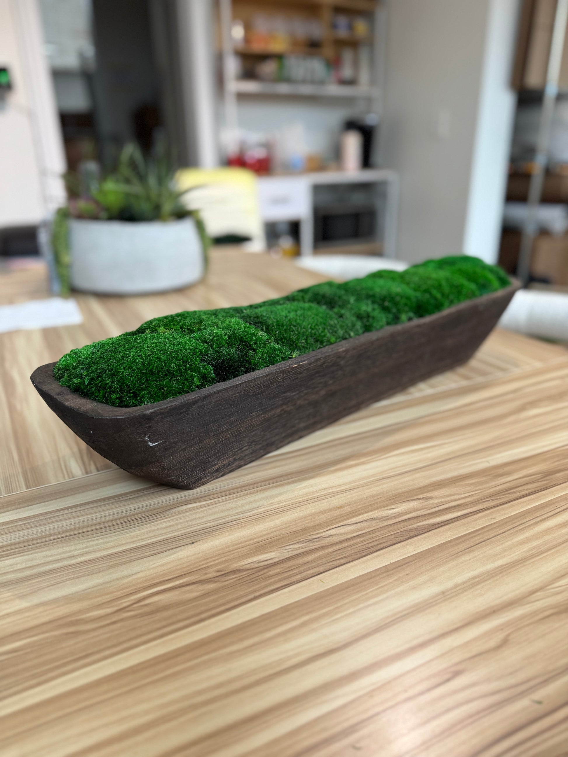 Moss-filled wooden planter on a wooden table with a blurred kitchen background